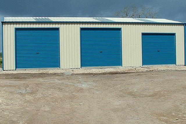 A cream building with three blue roller doors that are closed