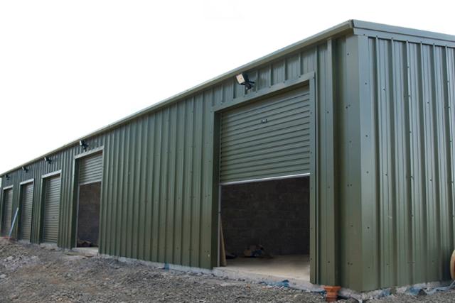 A green building with a roller door half-closed